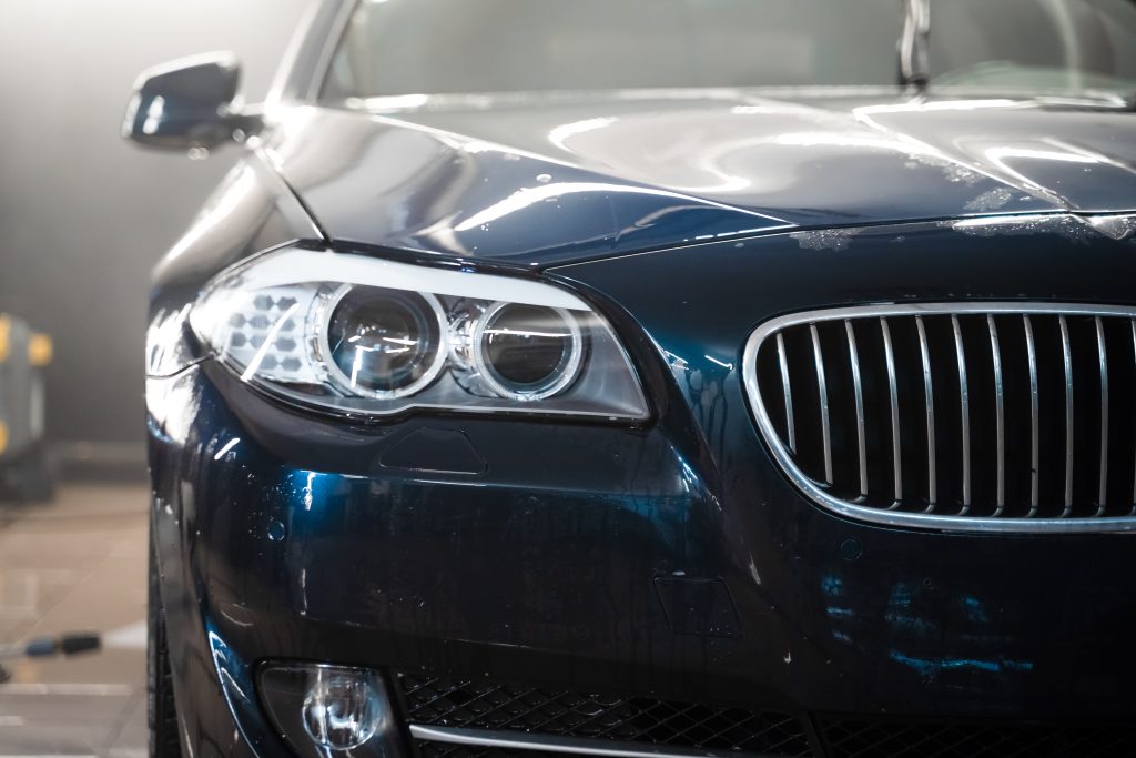 Close-up of a dark blue luxury sedan's front, showcasing sleek headlights and an elongated grille. Soft background lighting.