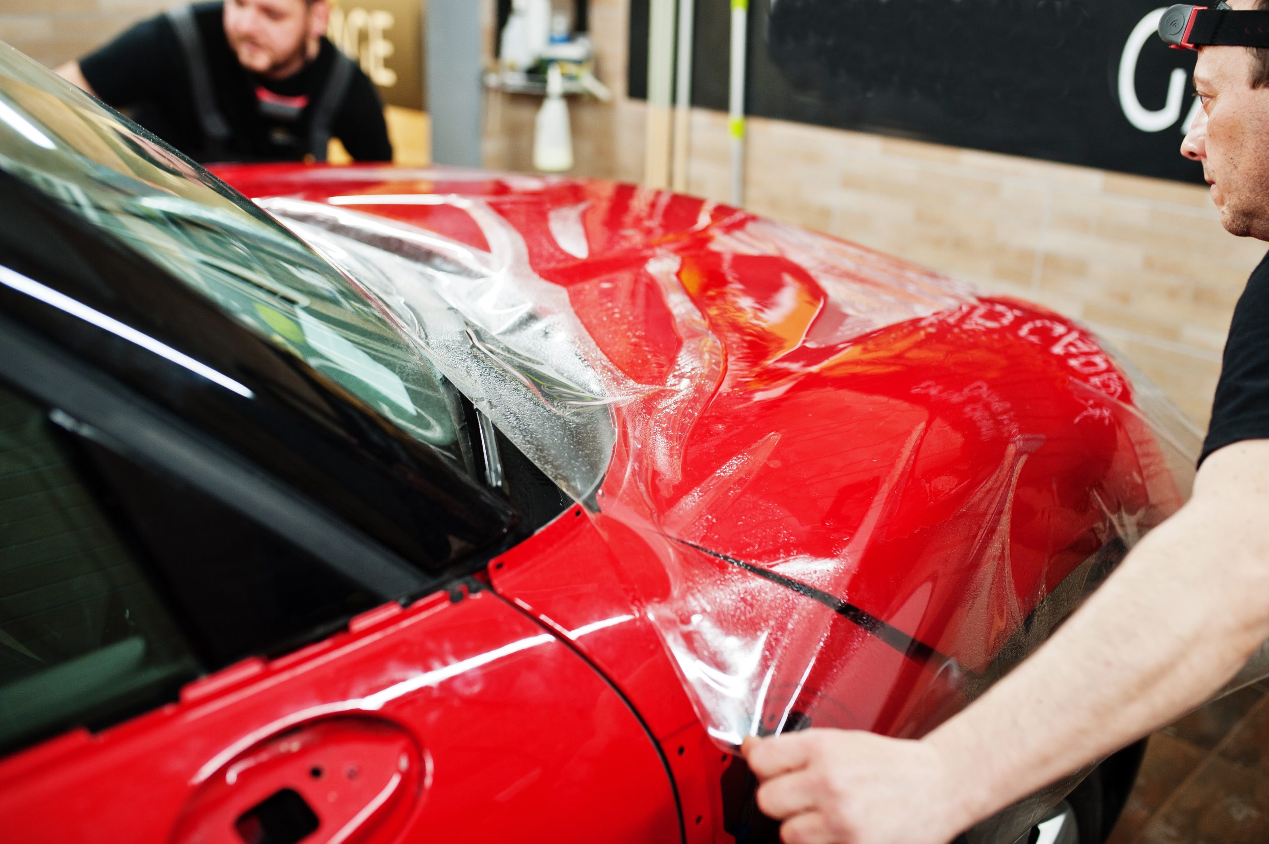 Two technicians apply paint protection film to a car's surface to protect it from scratches, chips, and UV damage.