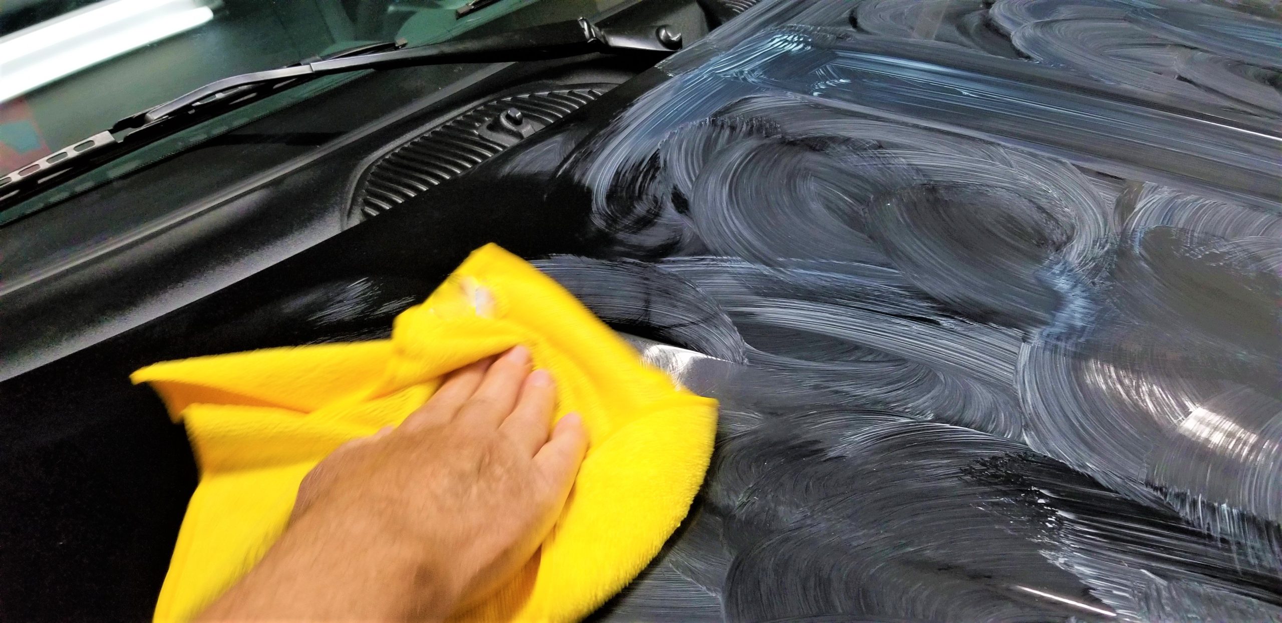 A professional auto detailer applying wax to a car’s hood